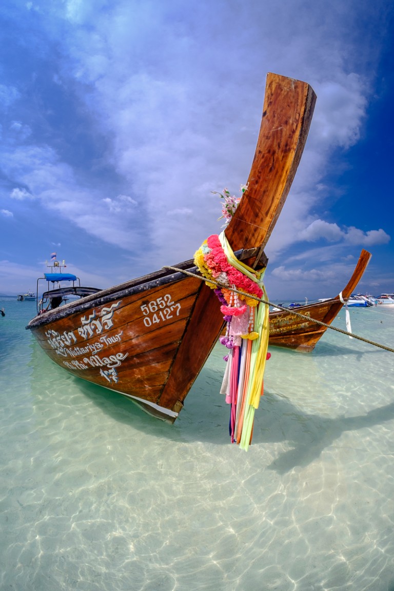 Traditional longtail boat with ribbons on its bow in clear water in Thailand
