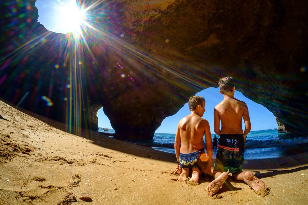 Two children sitting on the sand inside the Benagil Sea Cave as sunlight streams through the roof