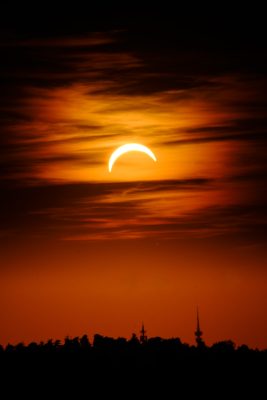 Crescent sun above towers silhouetted on the horizon at sunset during the eclipse