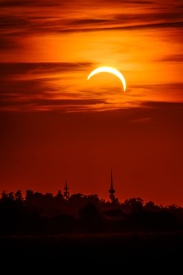 Partially eclipsed sun as a bright crescent over a dark skyline at dusk