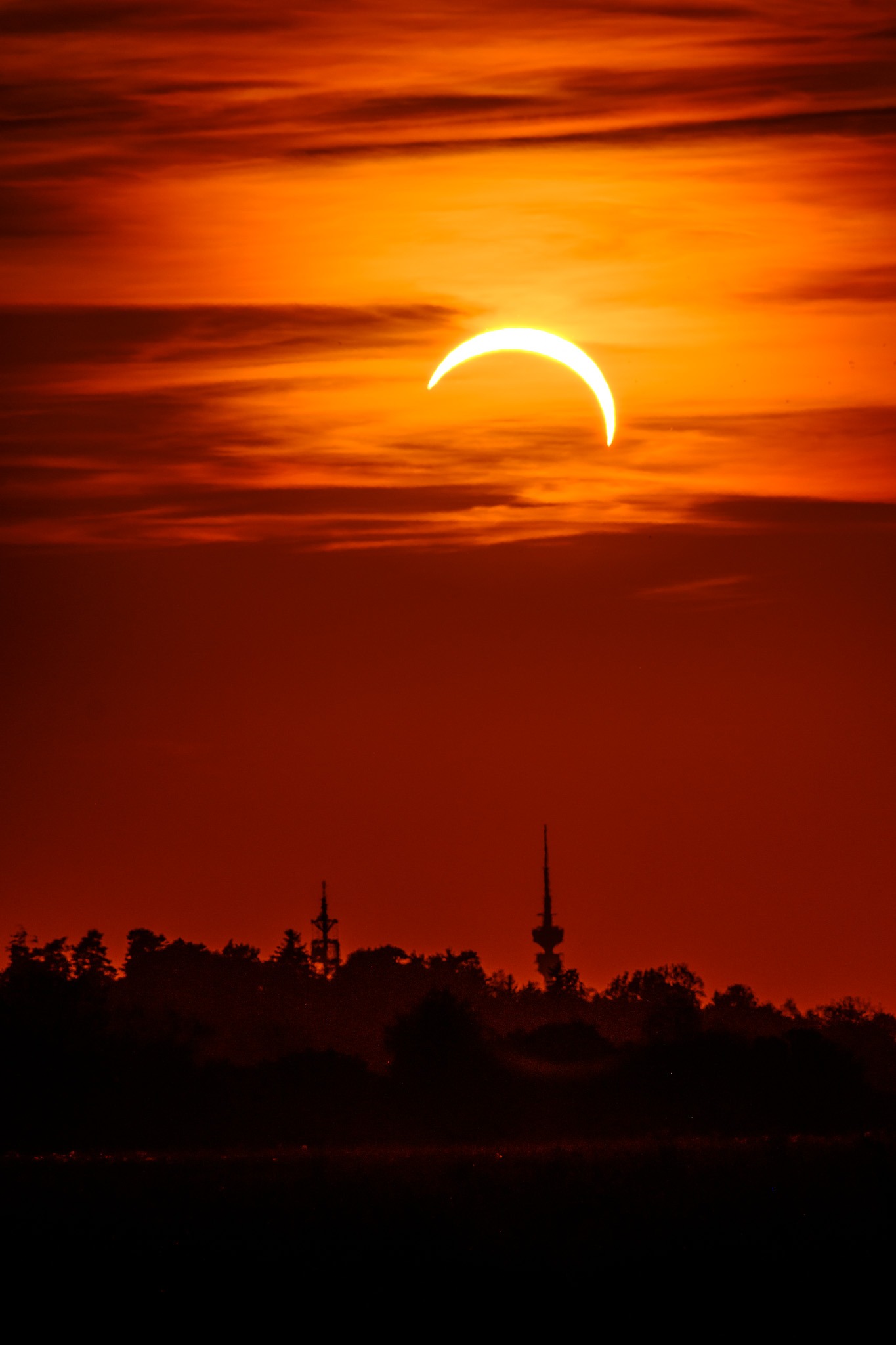Partially eclipsed sun as a bright crescent over a dark skyline at dusk